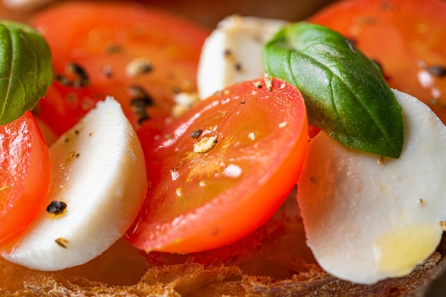 Bruschetta caprese. feuilles de basilic frais, tomates aromatiques mûres et mozzarella italienne sur bruschetta, arrosées d'huile d'olive et saupoudrées de poivre et d'herbes.