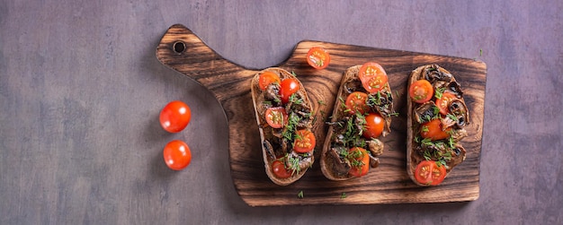 Bruschetta sur ciabatta de seigle avec tomates cerises et champignons frits sur une bannière web vue de dessus de plaque