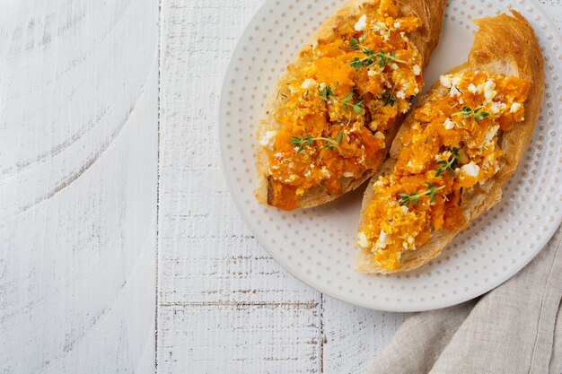 Bruschetta avec citrouille au four, fromage feta et thym sur une surface en bois clair