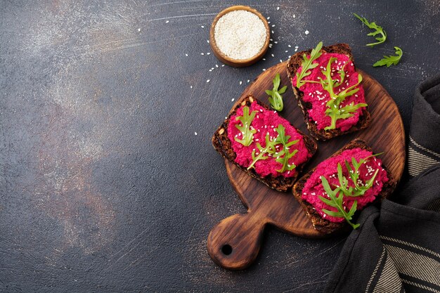 Bruschetta avec houmous de betterave, roquette et graines de sésame sur une surface de béton sombre