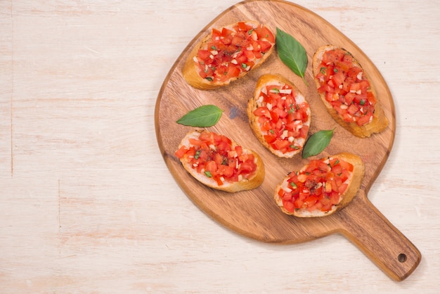 Bruschetta italienne avec tomates rôties, fromage mozzarella et herbes sur une planche à découper