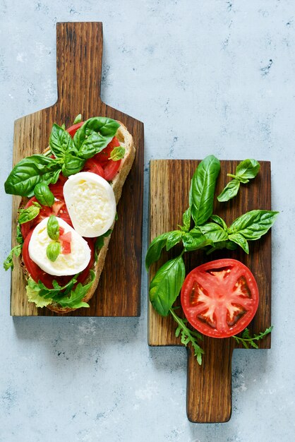 Bruschetta avec mozzarella buffalo cheese sur une planche à manger en bois avec des feuilles de tomate salsa de roquette et de basilic avec de l'huile d'olive sur un mur gris. Repas pour le déjeuner. Collation déjeuner, italien