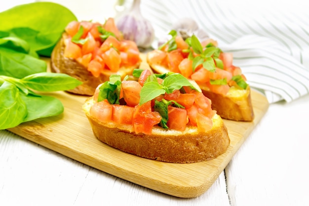 Bruschetta à la tomate, au basilic et aux épinards sur une assiette, feuilles d'épinards frais, serviette et huile végétale dans une carafe sur fond de planche de bois