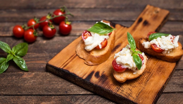 Bruschettas au fromage stracciatella tomates cerises et basilic sur planche à découper en bois