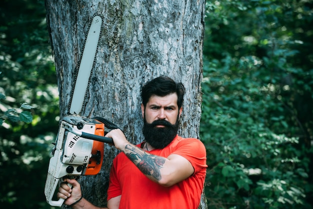 Bûcheron avec hache ou tronçonneuse dans la déforestation de la forêt d'été beau jeune homme avec hache près de ...