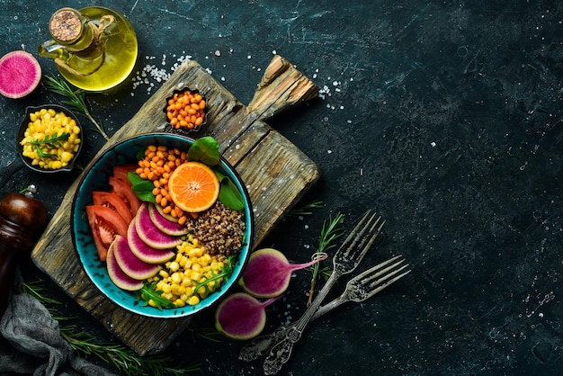 Buddha bowl : quinoa, épinards, maïs, tomates et radis pastèque, argousier. Manger végétarien sain, super nourriture. Vue de dessus Sur un fond de pierre.