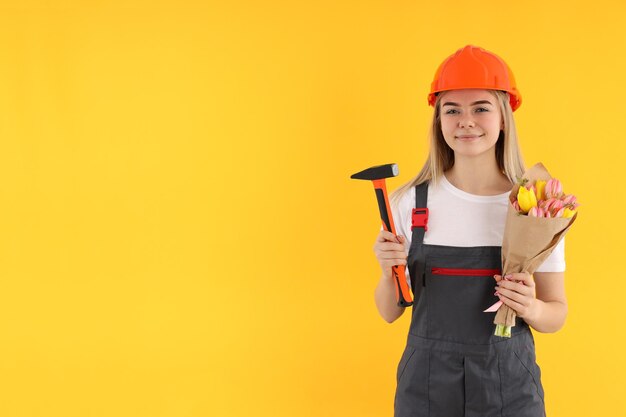 Builder femme avec bouquet et marteau sur fond jaune