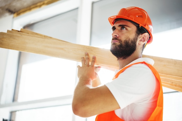 Builder man in hardhat transportant du bois sur chantier close up