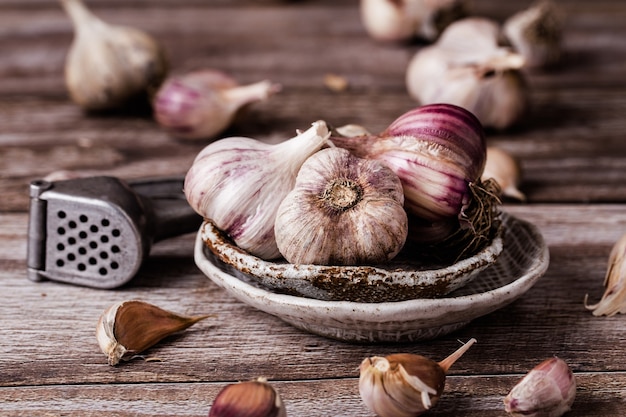 Les bulbes d'ail, en tranches, sur une plaque en céramique sur une table en bois, le presse-ail