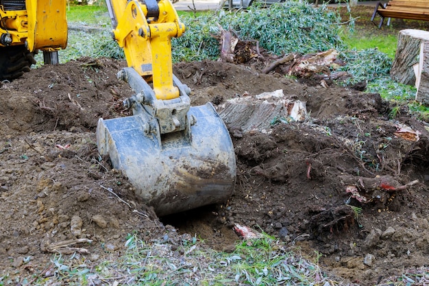 Bulldozer de travail de jardin nettoyant la terre des vieux arbres, des racines et des branches avec des machines de pelle rétro dans un quartier urbain.