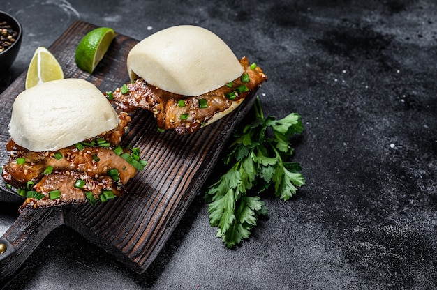 Bun bao cuit à la vapeur avec poitrine de porc et légumes. Fond noir.