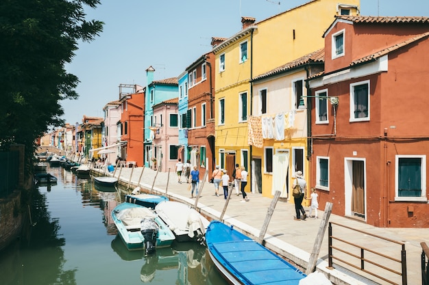 Burano, Venise, Italie - 2 juillet 2018 : Vue panoramique sur les maisons aux couleurs vives et le canal d'eau avec des bateaux à Burano, c'est une île de la lagune de Venise. Les gens marchent et se reposent dans les rues