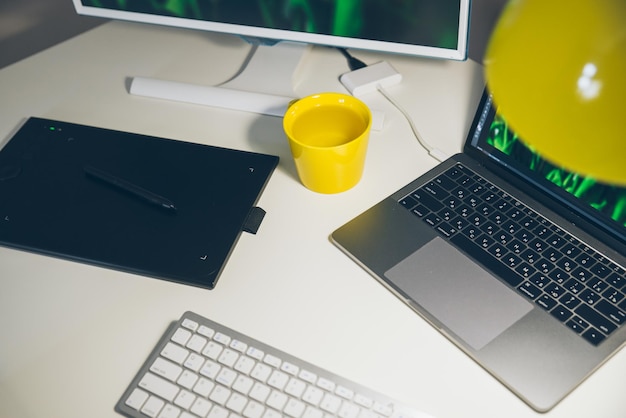 Bureau blanc de lieu de travail élégant avec ordinateur portable noir et tablette graphique et tasse jaune dessus