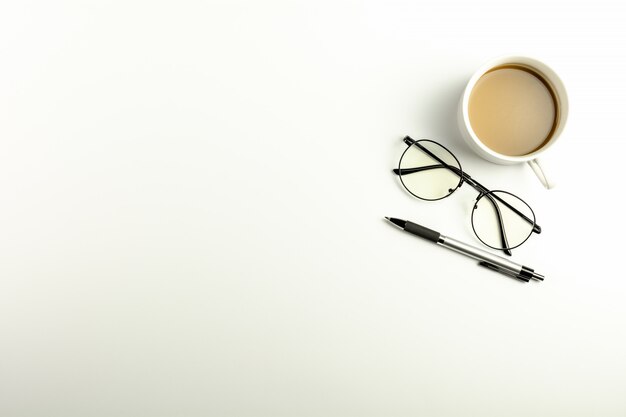 Bureau blanc avec des lunettes, un stylo et une tasse à café