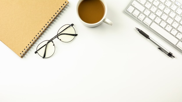 Bureau blanc moderne avec un clavier d&#39;ordinateur, un stylo, un cahier et une tasse de café.