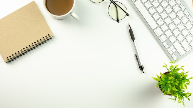 Bureau blanc moderne avec un clavier d&#39;ordinateur, un stylo, un cahier et une tasse de café.