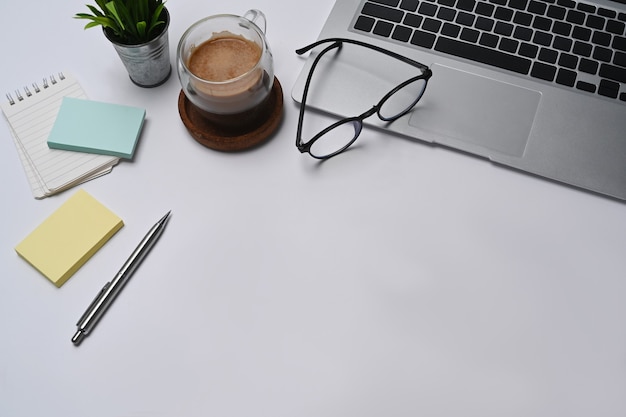 Bureau blanc avec ordinateur portable, notes autocollantes, verres et tasse à café.