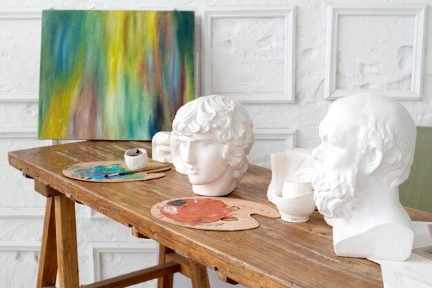 Bureau en bois du lieu de travail de l'artiste peintre avec des têtes de modèle en plâtre peindre des palettes et des pinceaux tachés