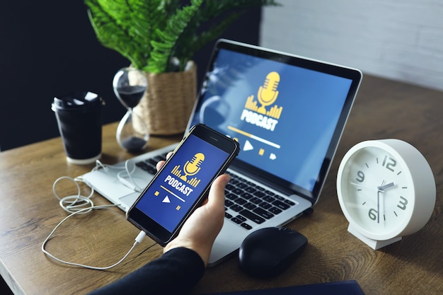 Bureau en bois avec un ordinateur portable avec service de site Web de podcast à l'écran. Main tenant un smartphone avec application de podcast.