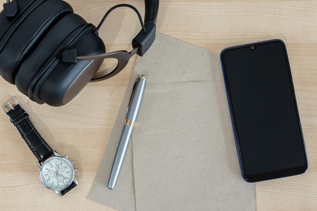 Bureau en bois vue de dessus avec un casque de téléphone intelligent, un stylo de montre et du papier recyclé
