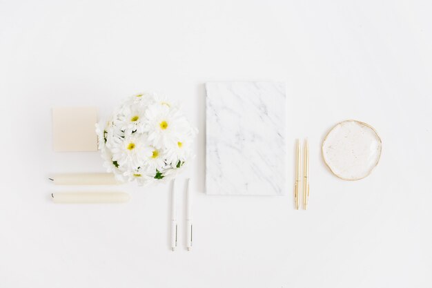 Bureau de bureau à domicile à plat. Espace de travail femme avec bouquet de fleurs de camomille et journal de marbre sur fond blanc. Vue de dessus