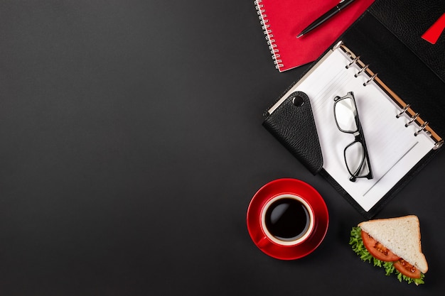 Bureau de bureau noir élégant avec ordinateur portable, tasse de café et un sandwich pour le déjeuner en vue de dessus