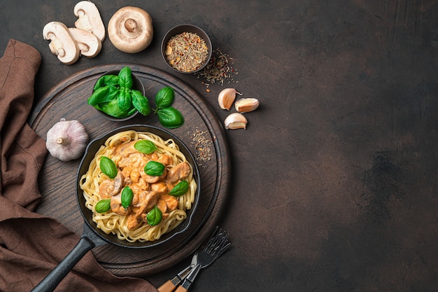 Bureau culinaire avec pâtes et sauce crémeuse aux champignons, basilic, ail et épices sur un bureau brun foncé. Vue de dessus, avec espace pour copier