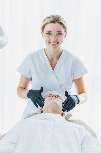 Bureau d'un dermatologue ou d'un cosmétologue travaillant avec des patientes assises à une table de massage massant le visage d'une jeune femme et faisant d'autres procédures pour la peau du visage Soins de la peau du visage