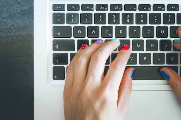 Photo bureau à domicile ou achats en ligne les doigts d'une femme aux ongles colorés tapent sur un clavier d'ordinateur portable