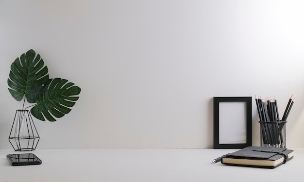 Bureau à domicile avec cadre photo de papeterie et plante en pot sur table blanche Espace de copie