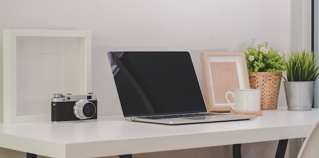 Bureau à domicile confortable avec ordinateur portable à écran blanc ouvert avec appareil photo vintage et fournitures de bureau