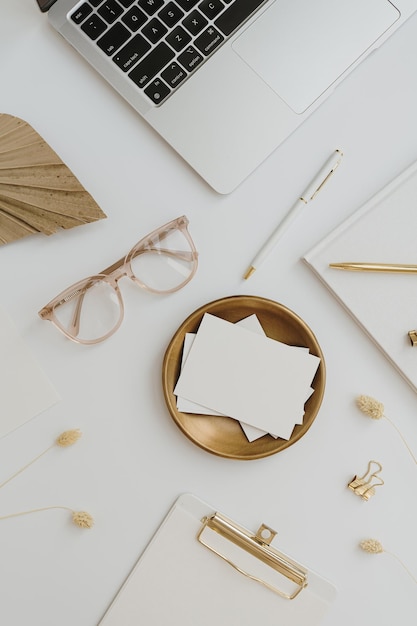 Bureau à domicile espace de travail avec ordinateur portable feuille de carte de papier vierge avec fond lunettes papeterie sur table blanche vue de dessus à plat