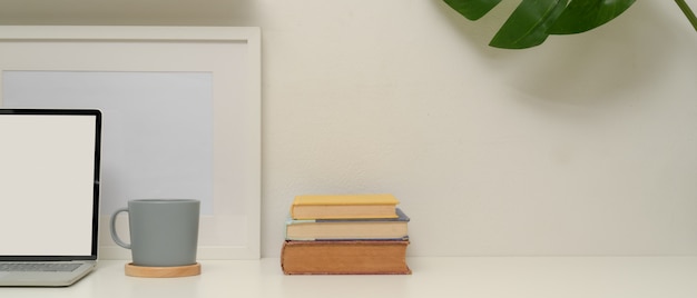 Bureau à domicile minimal avec maquette d'ordinateur portable, tasse, livres, cadre, maison de l'usine et espace de copie sur tableau blanc