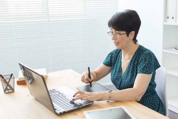 Bureau, graphiste, numérique - femme d'âge moyen travaillant au bureau avec ordinateur portable et numérique