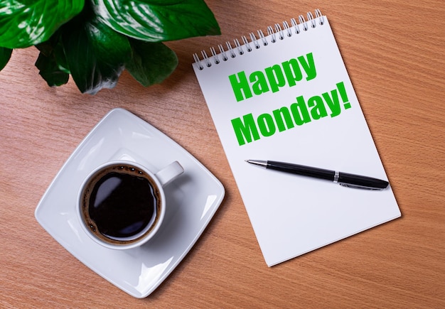 Sur le bureau, il y a une plante verte une tasse de café blanche un stylo et un bloc-notes ouvert avec le texte HAPPY MONDAY Business concept Gros plan du lieu de travail