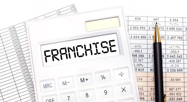 Sur le bureau, il y a des rapports, une calculatrice blanche avec le texte FRANCHISE sur le tableau de bord et un stylo. Concept d'entreprise.