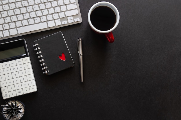 Bureau noir avec ordinateur portable, smartphone et autres fournitures de travail avec une tasse de café. Vue de dessus avec espace de copie pour la saisie du texte. Espace de travail design sur les éléments essentiels de la table de bureau à plat.