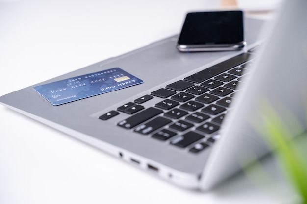 Photo bureau de paiement en ligne, restez à la maison pour faire du shopping, paiement électronique avec concept de carte de crédit, ordinateur portable sur fond de tableau blanc avec panier de magasin, gros plan.