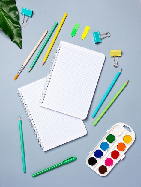 Bureau à plat avec une page vierge d'un cahier avec un stylo, des crayons, de l'aquarelle et d'autres articles de papeterie Vue de dessus à plat