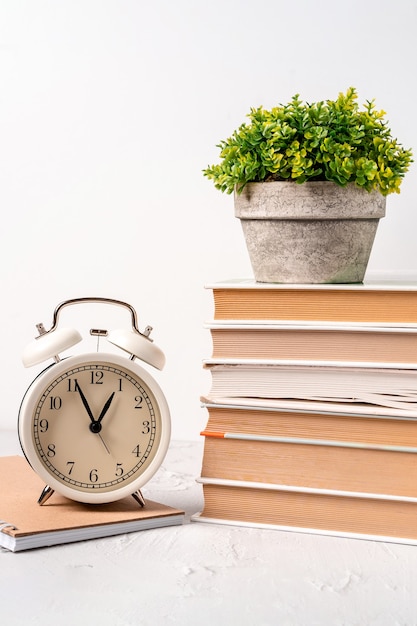 Bureau avec réveil et une pile de livres et plante verte. Temps de travail conceptuel