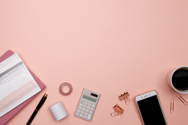 Bureau de table de bureau avec smartphone et autres fournitures de bureau sur fond rose.