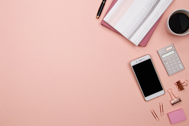 Bureau de table de bureau avec smartphone et autres fournitures de bureau sur fond rose.