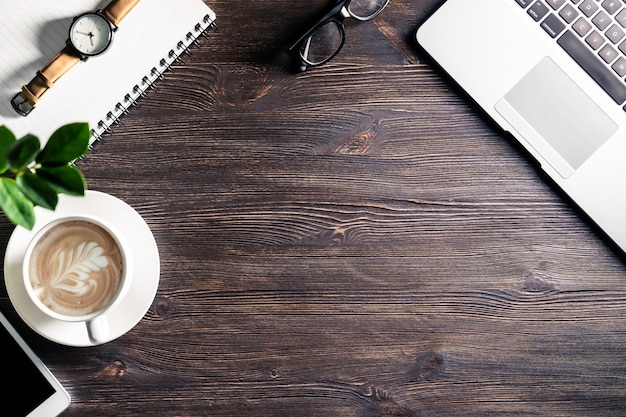 Bureau de travail d'affaires avec des lunettes de stylo pour ordinateur portable et téléphone portable regarder sur une table en bois sombre, fond de table de travail moderne avec des appareils et une tasse de café, vue de dessus d'en haut