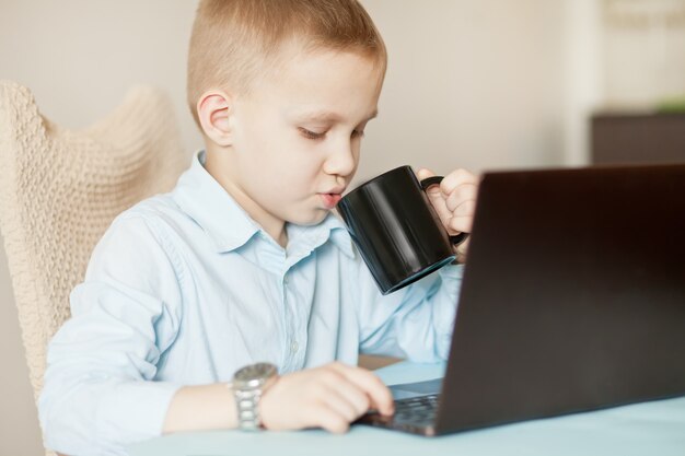 Bureau de travail avec ordinateur portable. Garçon d'affaires assis à table et boire une tasse de café. Enfant apprenant en ligne. Enseignement à distance en ligne.