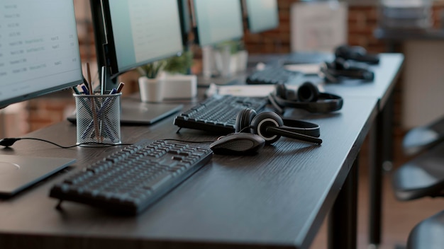 Bureau vide avec plusieurs moniteurs et gadgets modernes utilisés pour la discussion du centre d'appels avec les clients sur la ligne d'assistance. Aucune personne au poste de travail avec clavier, souris, ordinateurs et écouteurs. Fermer.