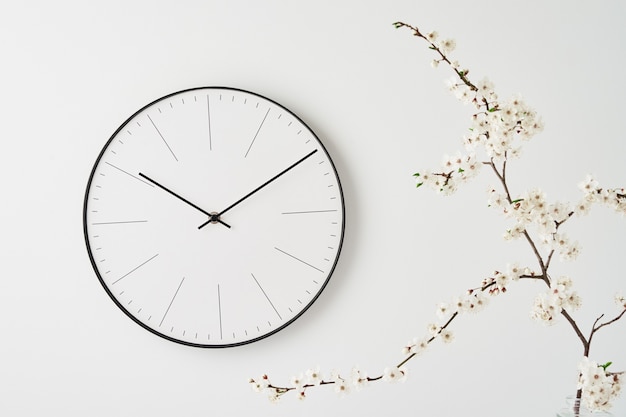 Bureau de vue avant avec horloge murale et branche d'usine sur fond blanc. Style de décoration minimal