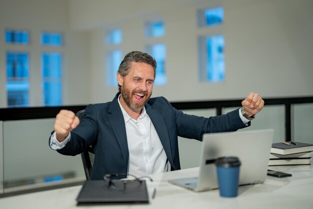 Photo des bureaux d'affaires un homme d'affaires excité travaillant avec un ordinateur portable au bureau un directeur d'entreprise utilisant un ordinateur laptop un gestionnaire de la génération du millénaire sur le lieu de travail des employés de bureau des hommes d'affaires au bureau