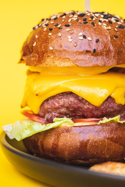 Burger appétissant avec escalope de boeuf et beaucoup de fromage sur fond jaune. Pomme de terre croustillante dorée