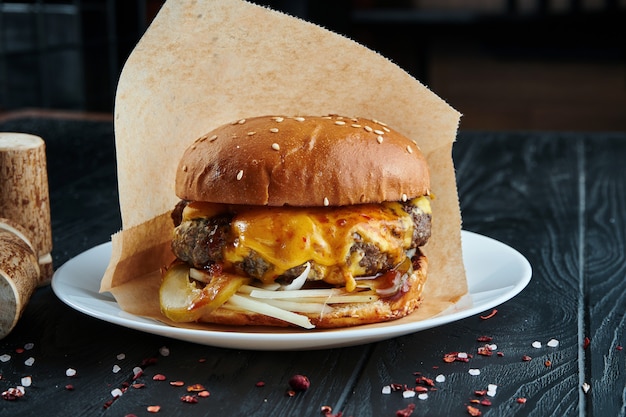 Burger appétissant et juteux avec une grande galette de boeuf, des concombres marinés, de la sauce et du chou blanc sur une assiette blanche avec des frites. Fermer. Espace copie