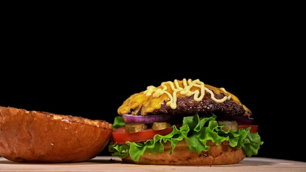 Le burger artisanal cuisine sur fond noir dans des gants de cuisine noirs Se compose de sauce laitue tomate oignon rouge cornichon fromage bacon air bun et viande de boeuf marbrée